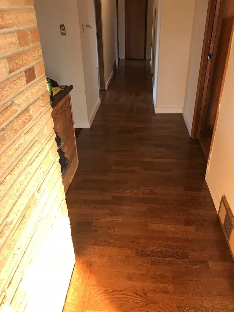 A hallway with hardwood floors and a brick wall.