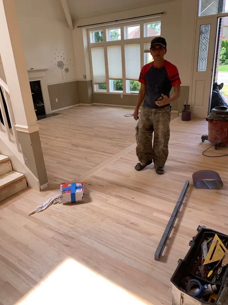 A man is standing on a wooden floor in a living room.