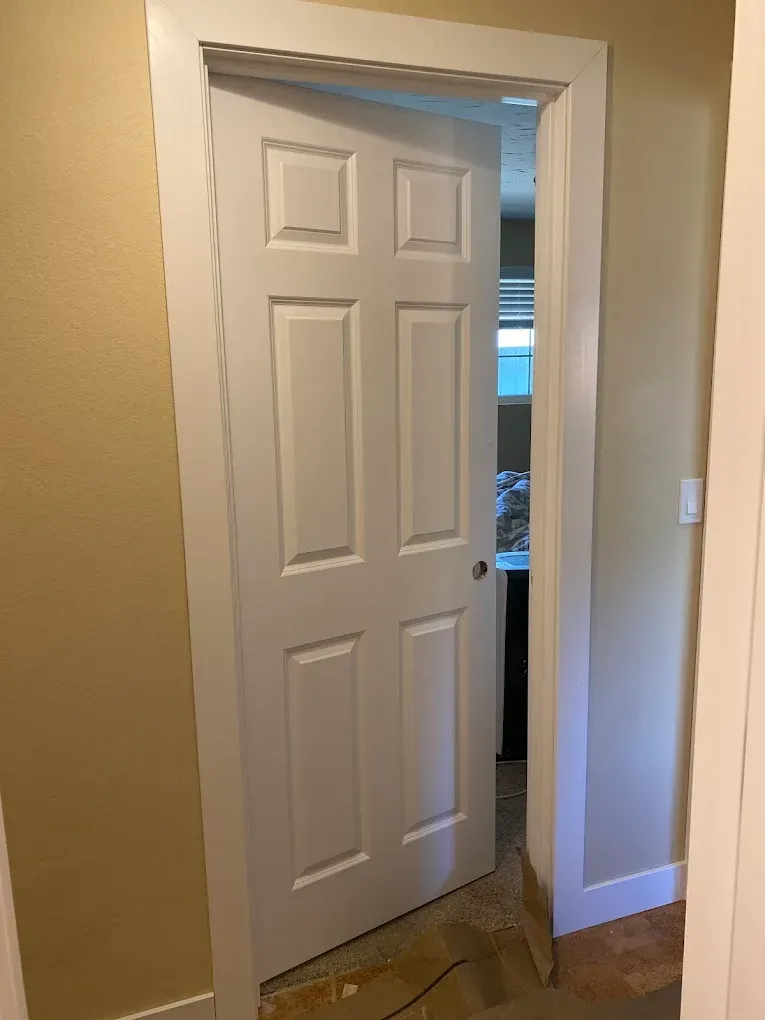 A white door is open in a hallway leading to a kitchen.