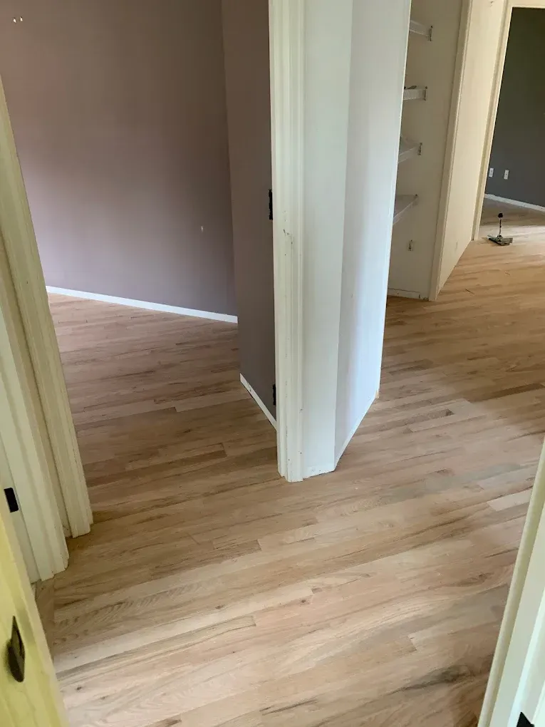A hallway with hardwood floors between two rooms in a house.