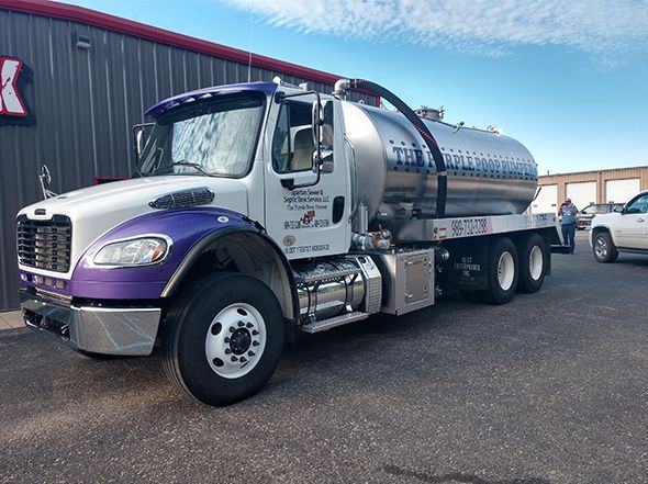 A green industrial hose inserted into an open, circular underground tank, next to a metal manhole cover in a yard.