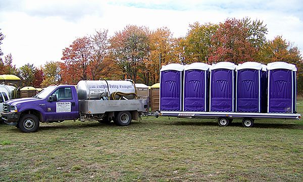 A new home under construction with dark blue siding, a garage, and a portable toilet on a dirt lot with gravel.
