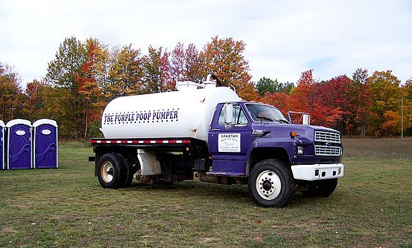 Two workers in protective gear inspect an open utility manhole in a grassy field, one holding a document.