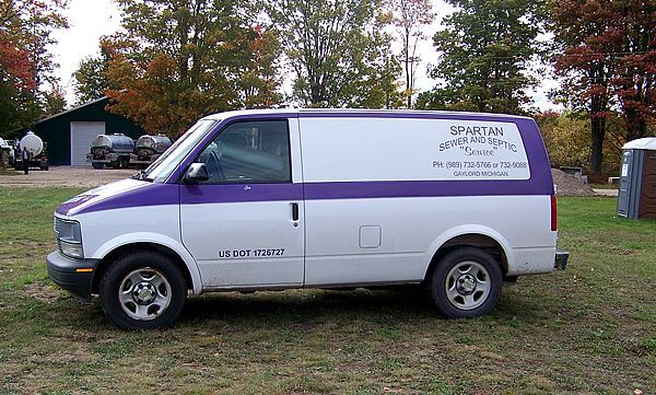 A white and purple utility van parked on a grass field near trees and a building.