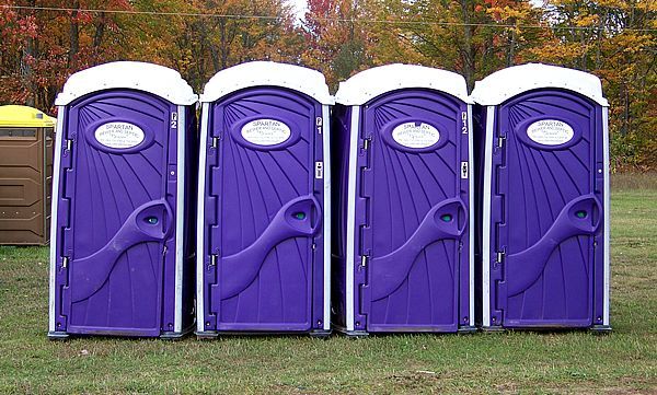 A long row of green portable toilets standing on an asphalt surface.