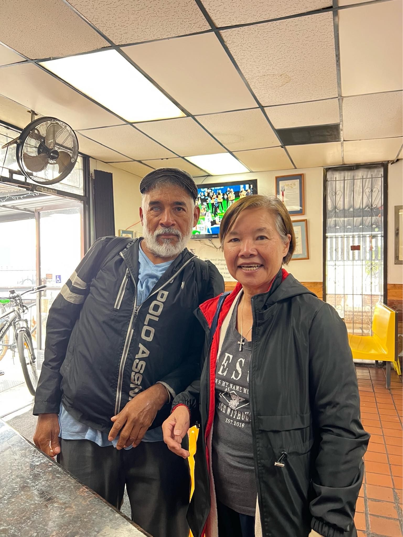 Two people stand side-by-side in a restaurant, smiling for a photo under indoor lighting.