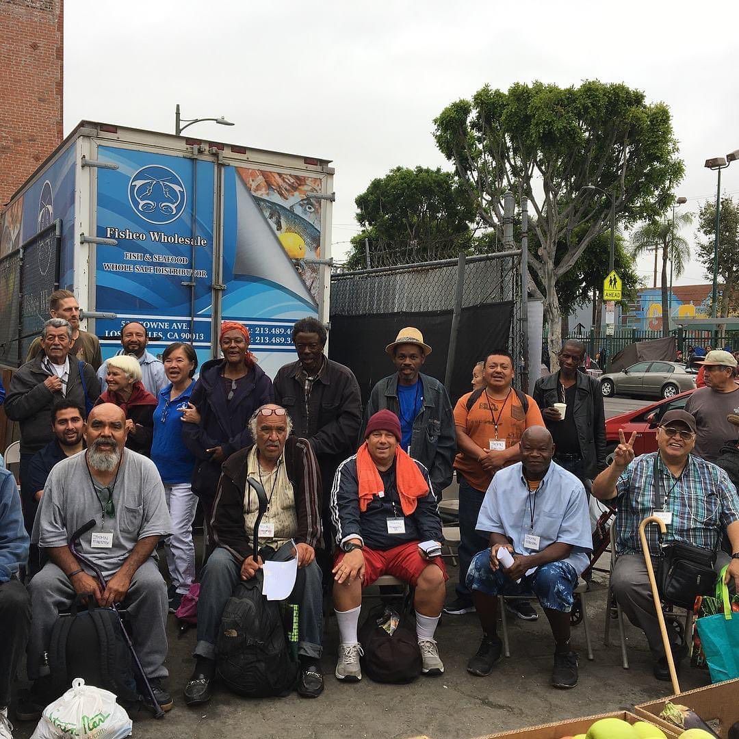 A diverse group of people posing for a photo in front of a blue and white supply truck on an overcast day.