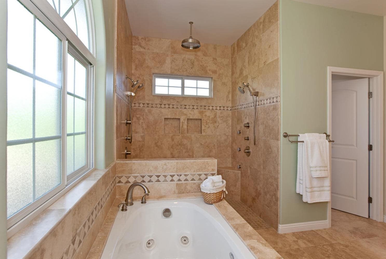 Luxurious bathroom with soaking tub, stone tile, shower, and arched window.