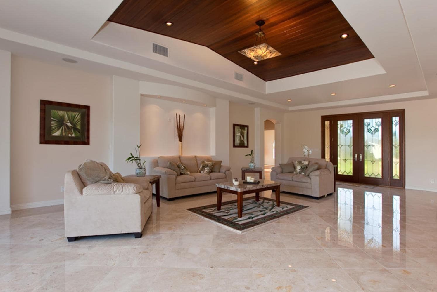 Spacious living room with beige marble floor, cream walls, dark wood ceiling detail, and seating arrangement.