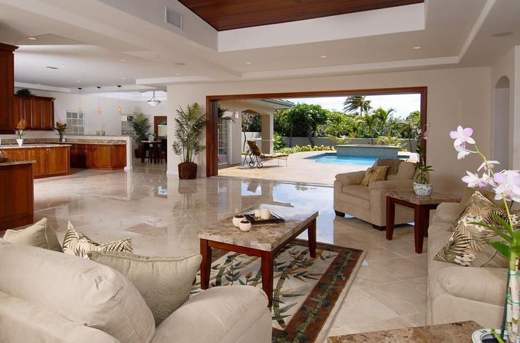 Spacious living room with open doors to a pool. Beige sofas, marble floors, and a wood-paneled ceiling.