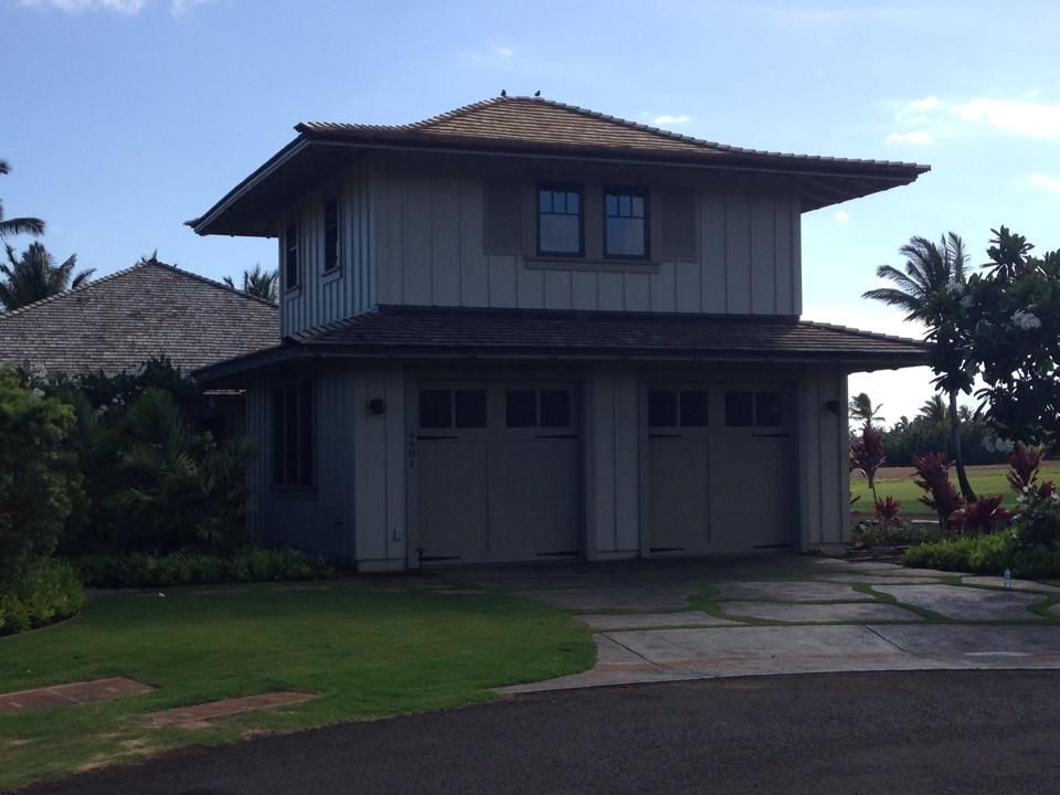 Two-story house with two garage doors and a brown roof, set on a green lawn.