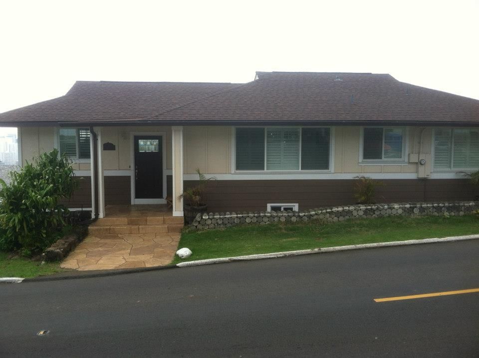 Beige and brown house with a tile roof, windows, and a paved walkway leading to the dark door.
