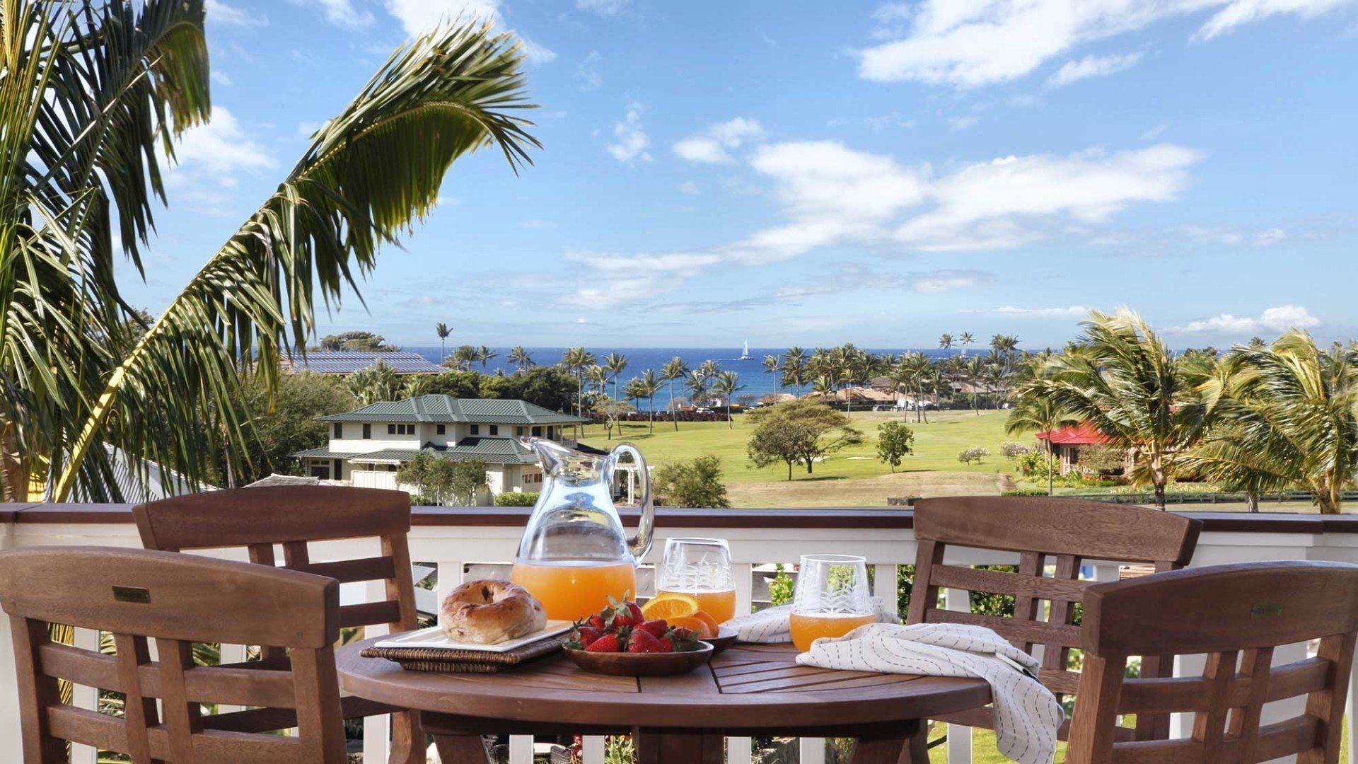 Patio table set for breakfast overlooking ocean. Orange juice, fruit, and bagels on table.