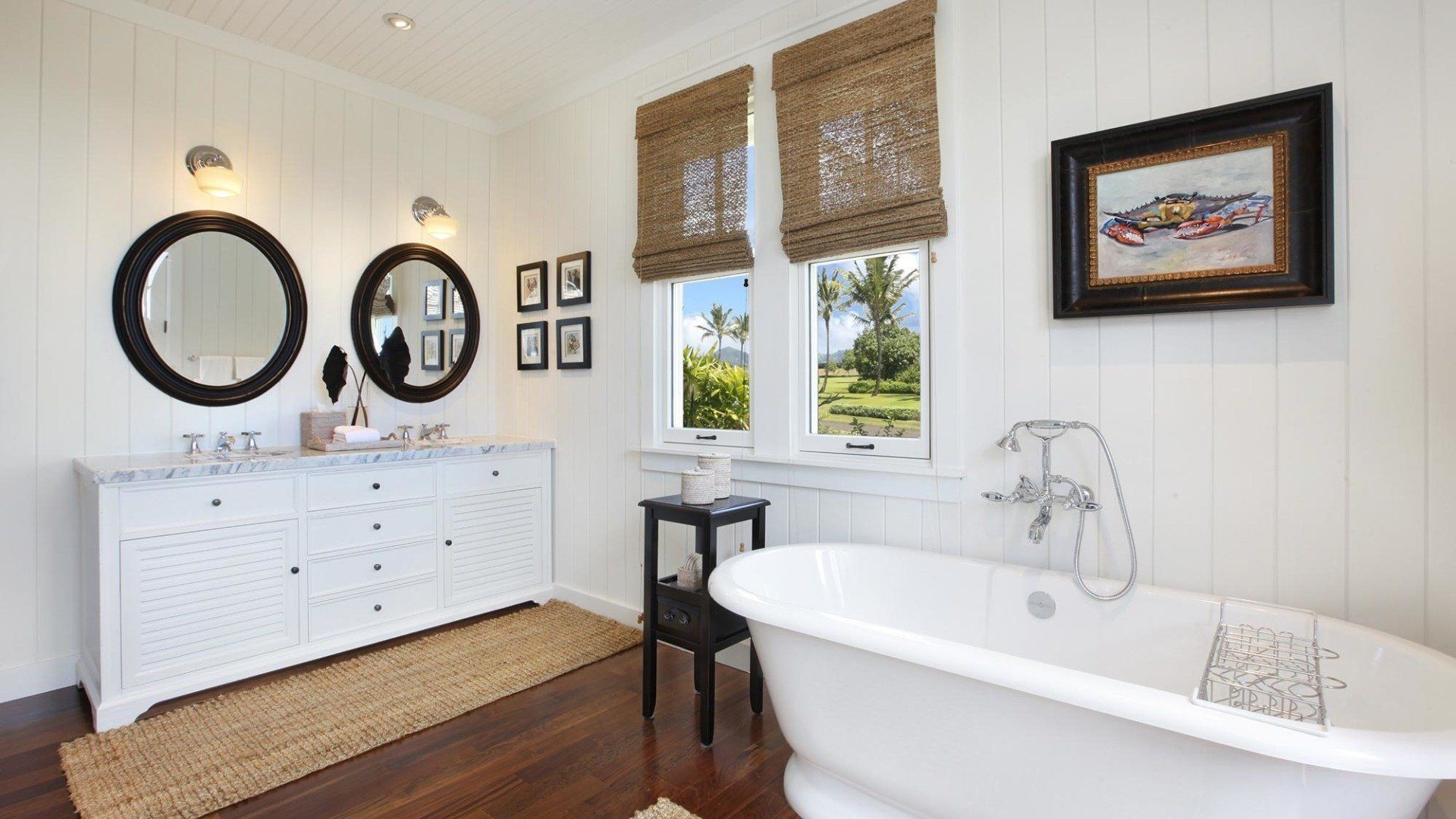 Bathroom with white walls, oval tub, double vanity, and woven shades on windows.