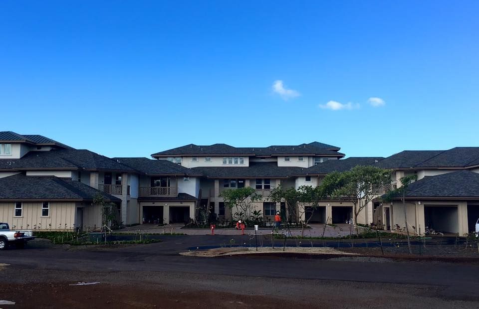 Multi-story residential complex with dark roofs, beige walls, and garages against a clear blue sky.