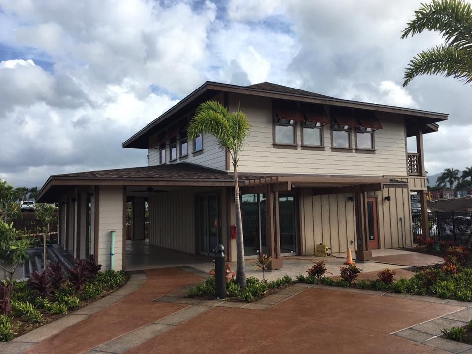 Two-story beige building with brown trim and a covered walkway. Palm tree and cloudy sky.