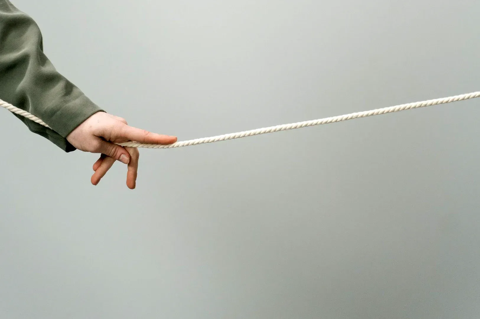 Minimalist photography of a hand holding a single, taut white rope against a neutral background, rep