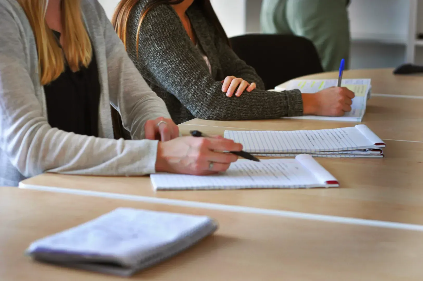 Students sitting at desks writing in notebooks, capturing the act of doing through note-taking and t