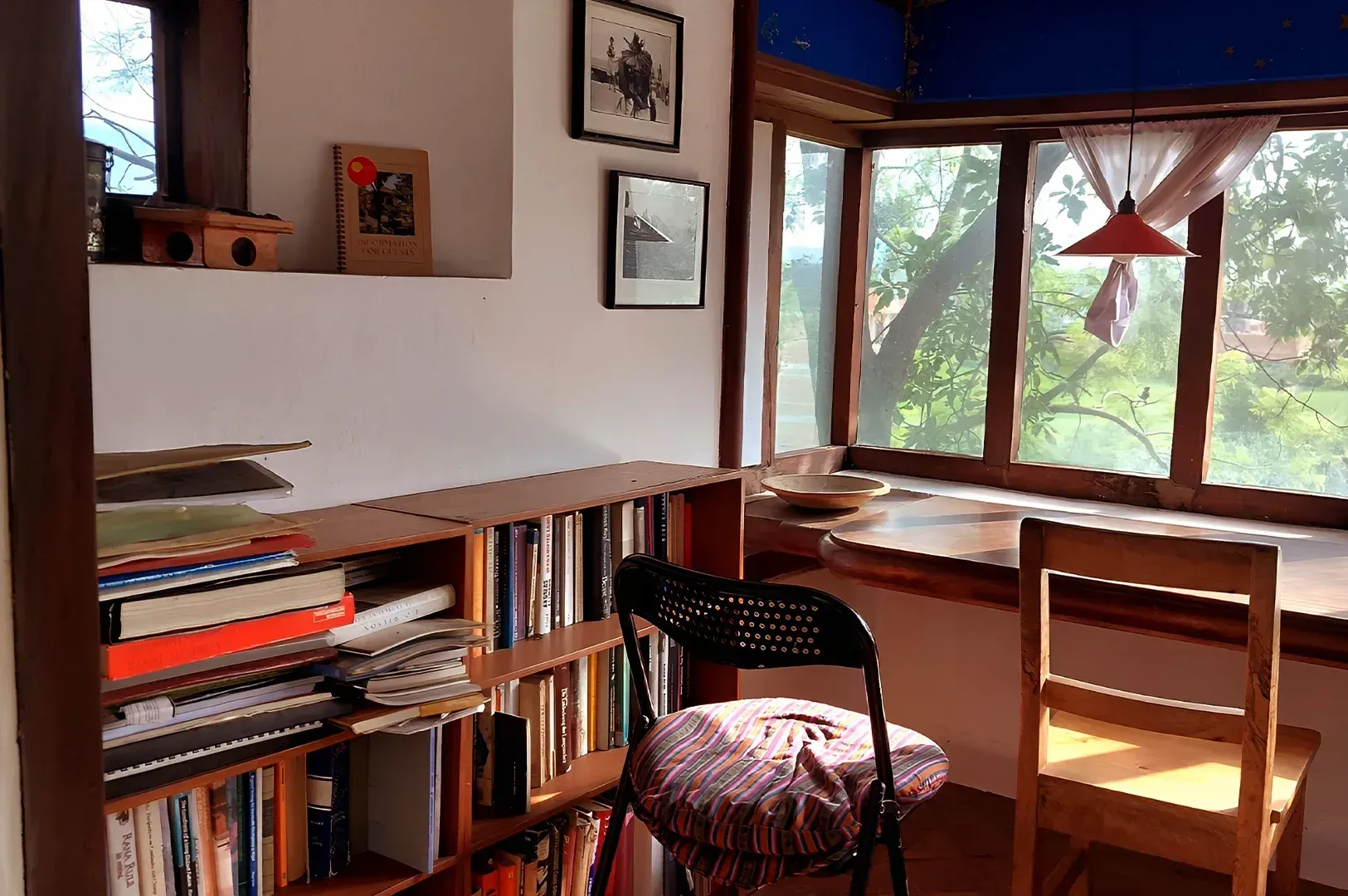 A serene, sunlit home studio corner featuring a wooden bookshelf, a cozy chair, and a large window l