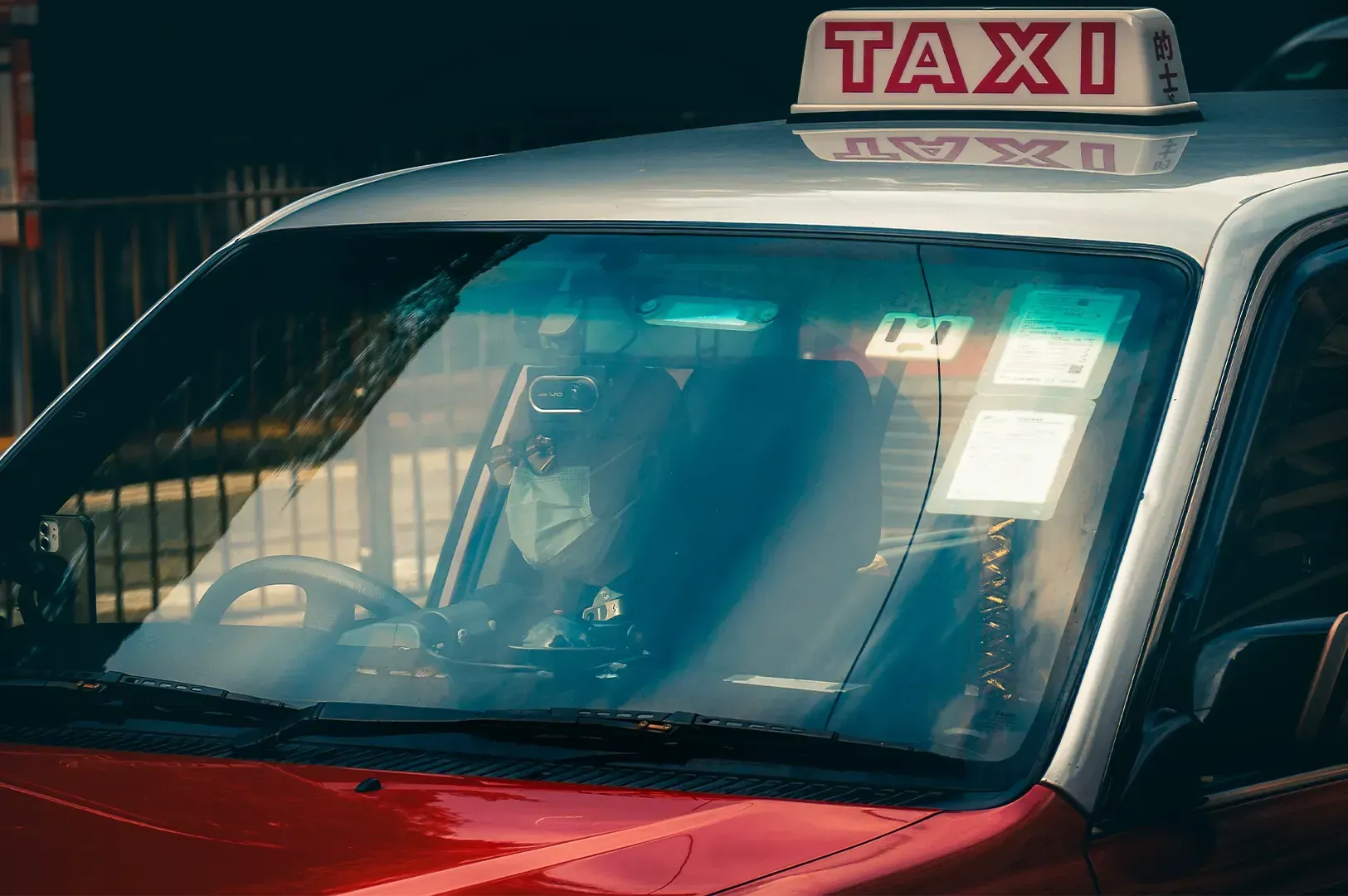 A close-up view of a taxi driver wearing a face mask inside a red taxi, capturing a candid moment of