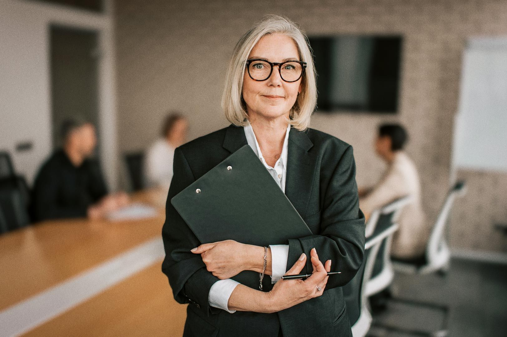 Authority figure in suit guiding workplace discussion, clipboard in hand, colleagues engaged around