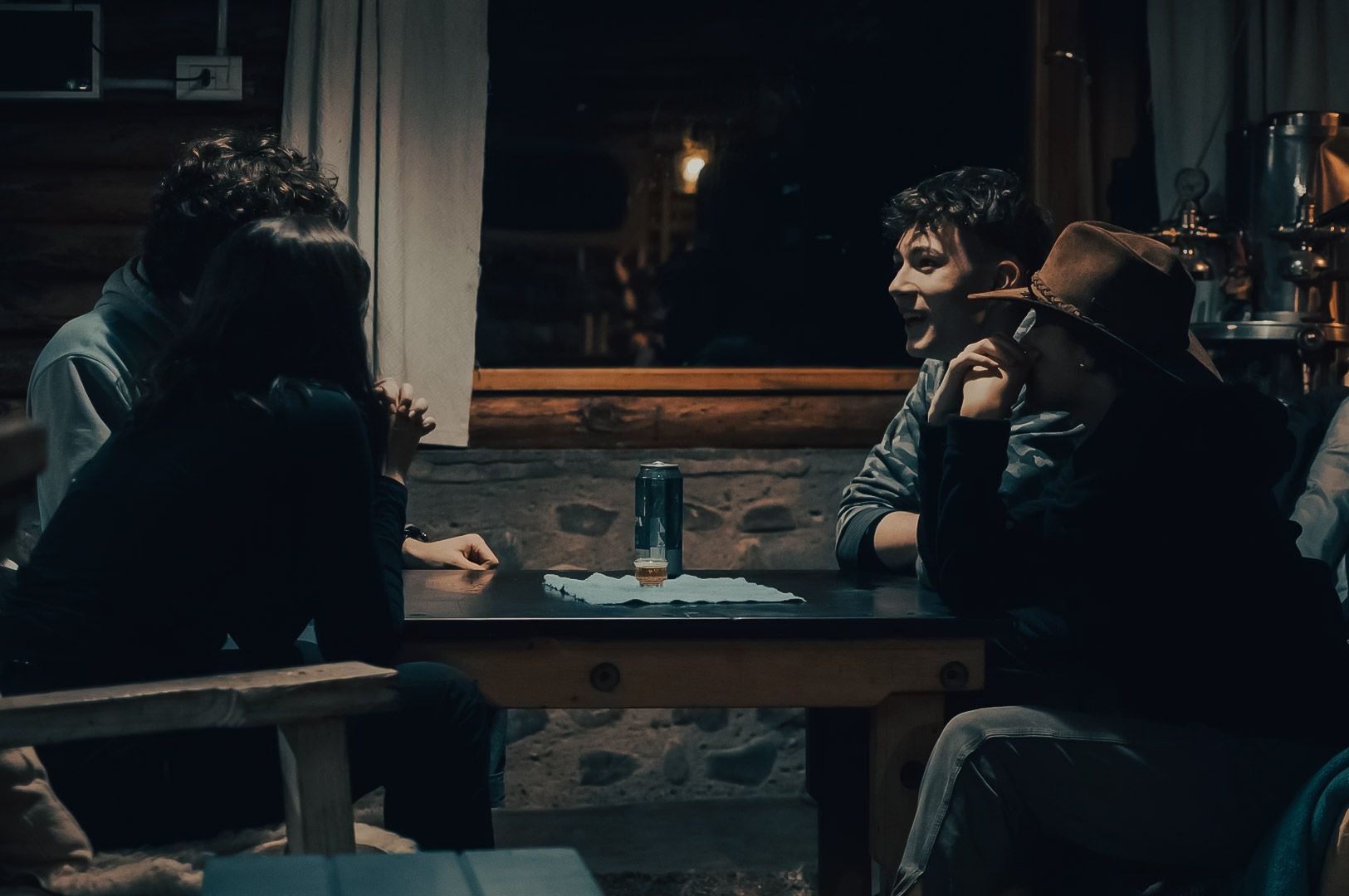 Group of friends having a deep conversation around a table in a cozy, dimly lit cabin.
