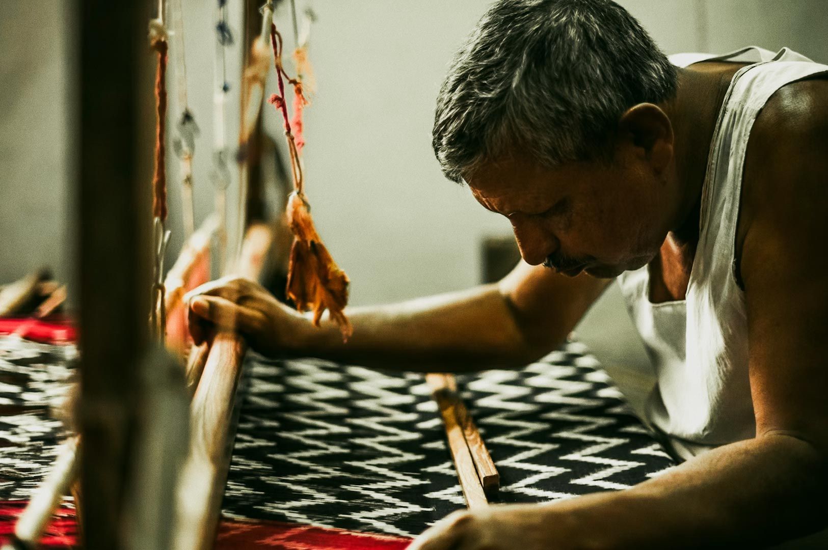 Traditional weaver at a handloom crafting a black-and-white zigzag textile with a red border.