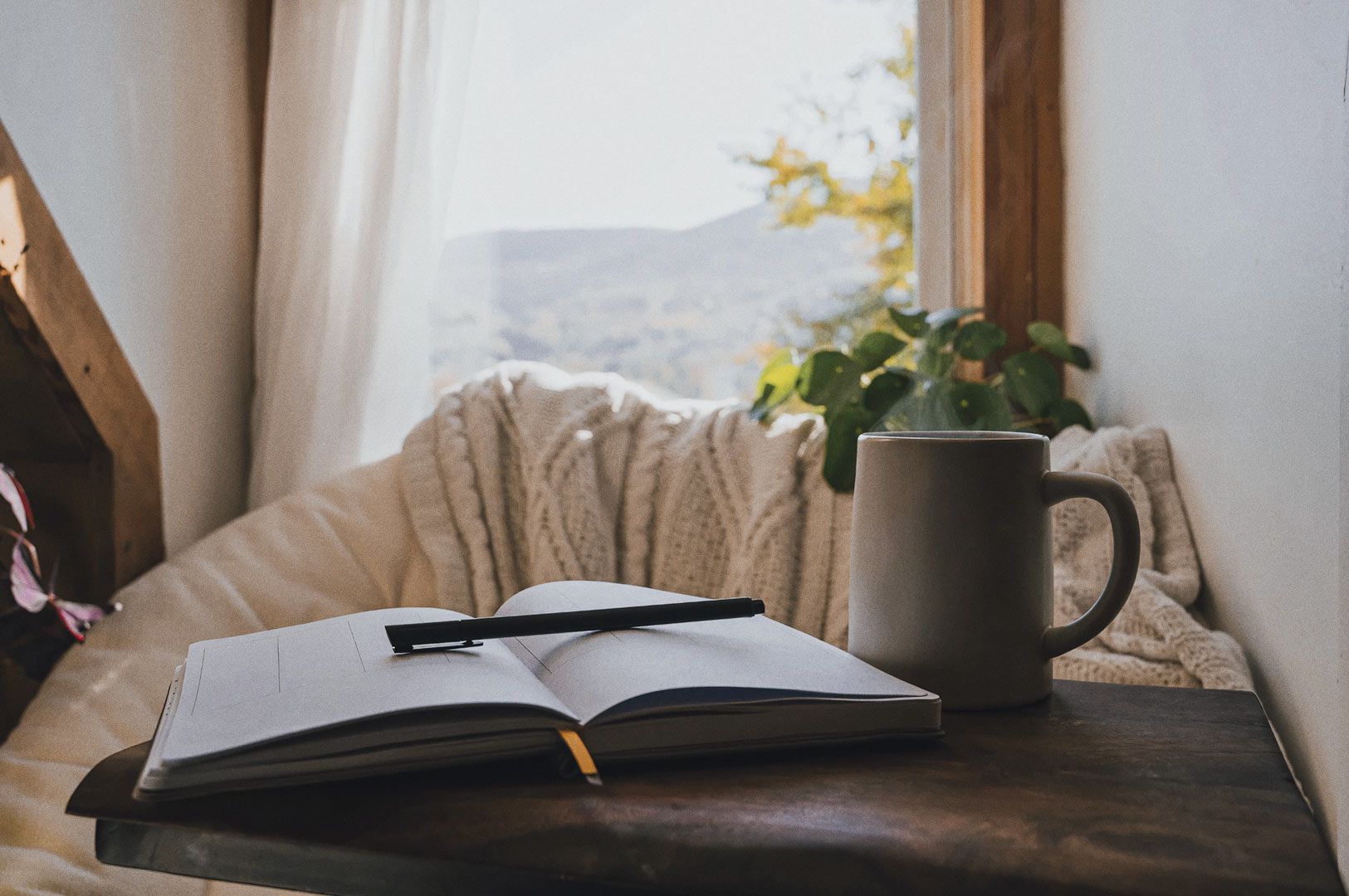 Relaxing corner with hot drink, open notebook, and autumn hills.