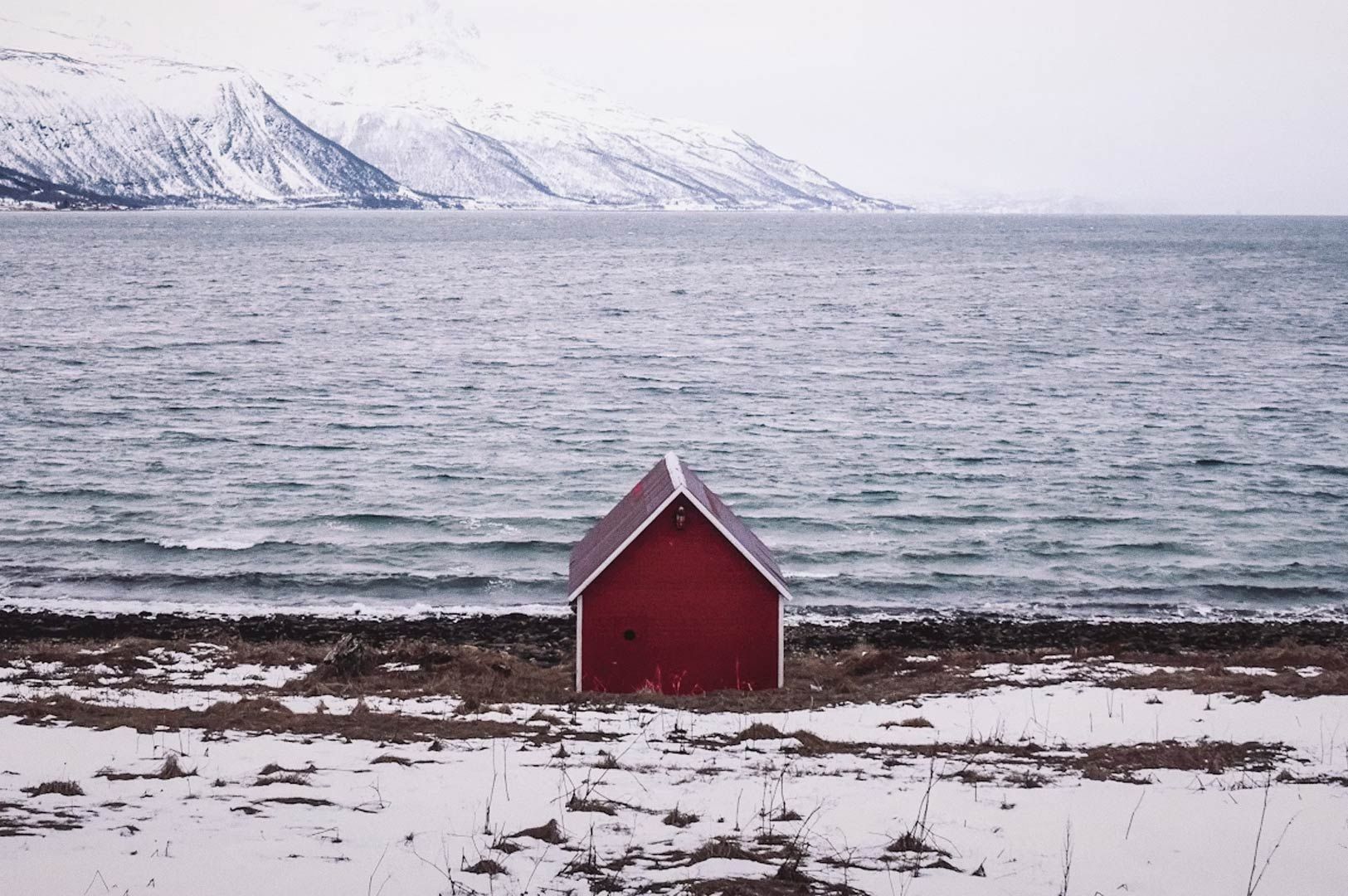 Red lighthouse on a rocky breakwater by the sea with a small boat nearby