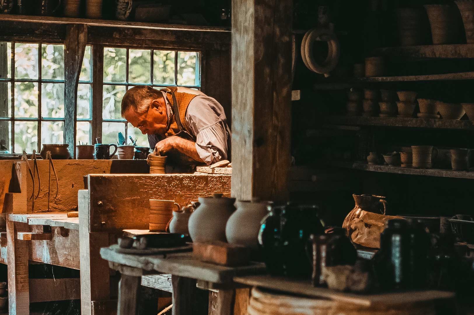 Artisan shaping clay pottery on a wheel inside a rustic workshop filled with handcrafted ceramic pie