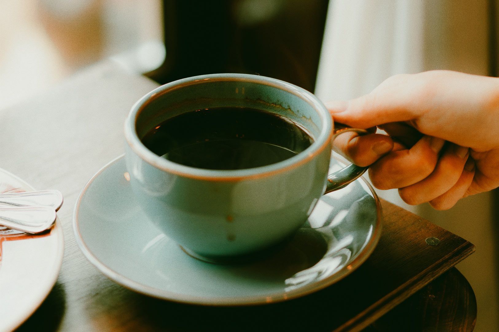 Hand holding a cup of black coffee in a ceramic mug.