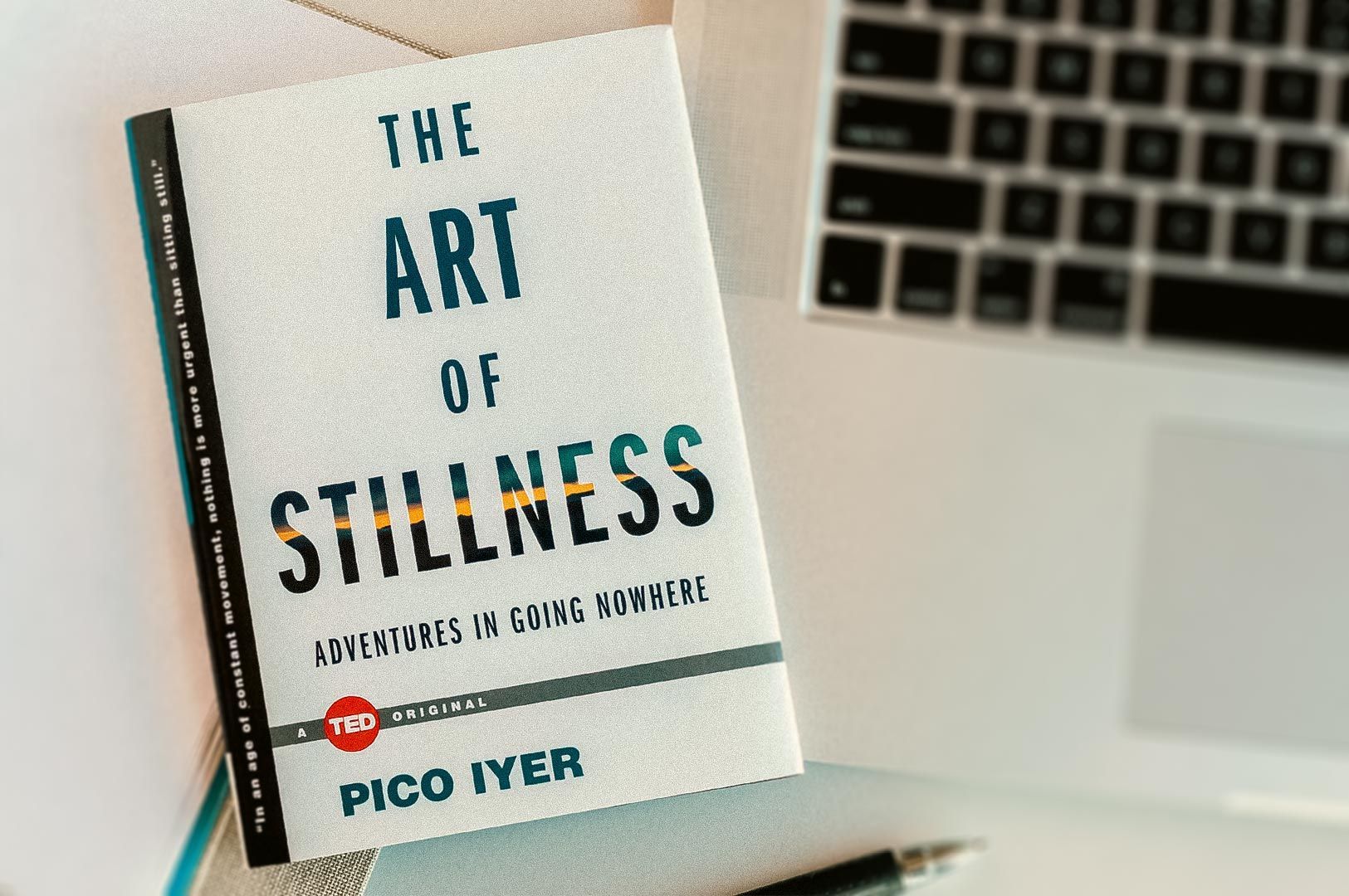 The book ‘The Art of Stillness’ by Pico Iyer placed beside a laptop in a calm, minimalist workspace.