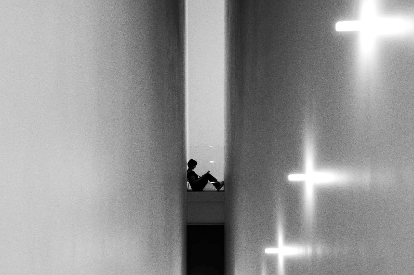 Image of a lone figure sitting in a slim vertical alley, leaning back with legs crossed, centered in