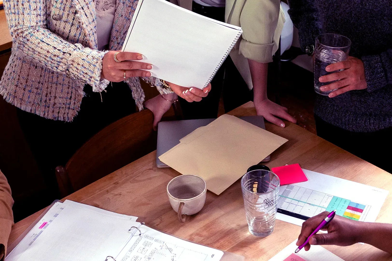 A group of professionals collaborating around a table with notebooks and documents, representing intentional companionship and the power of curated circles to tune one's life rather than just filling it.