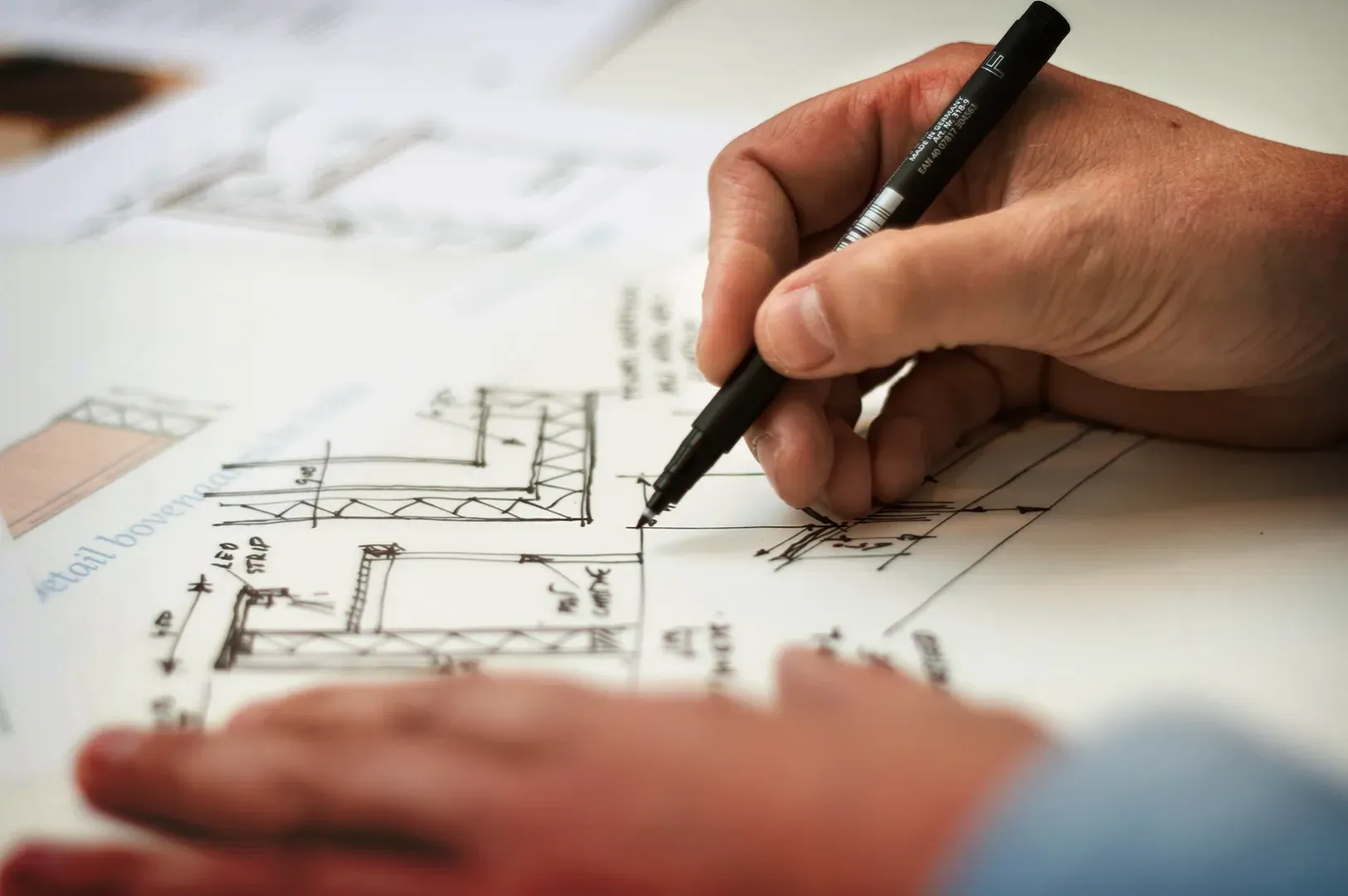 A focused shot of hands sketching detailed architectural plans, symbolizing the foundational role of deliberate practice, precision, and building mastery.