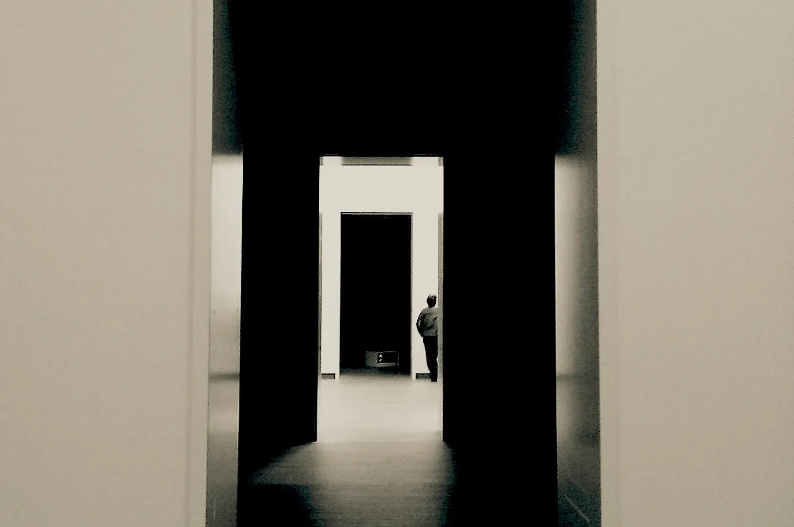 A minimalist, high-contrast perspective of a person walking through a series of doorways into a bright space, representing the long, methodical, and often solitary journey of building a startup.