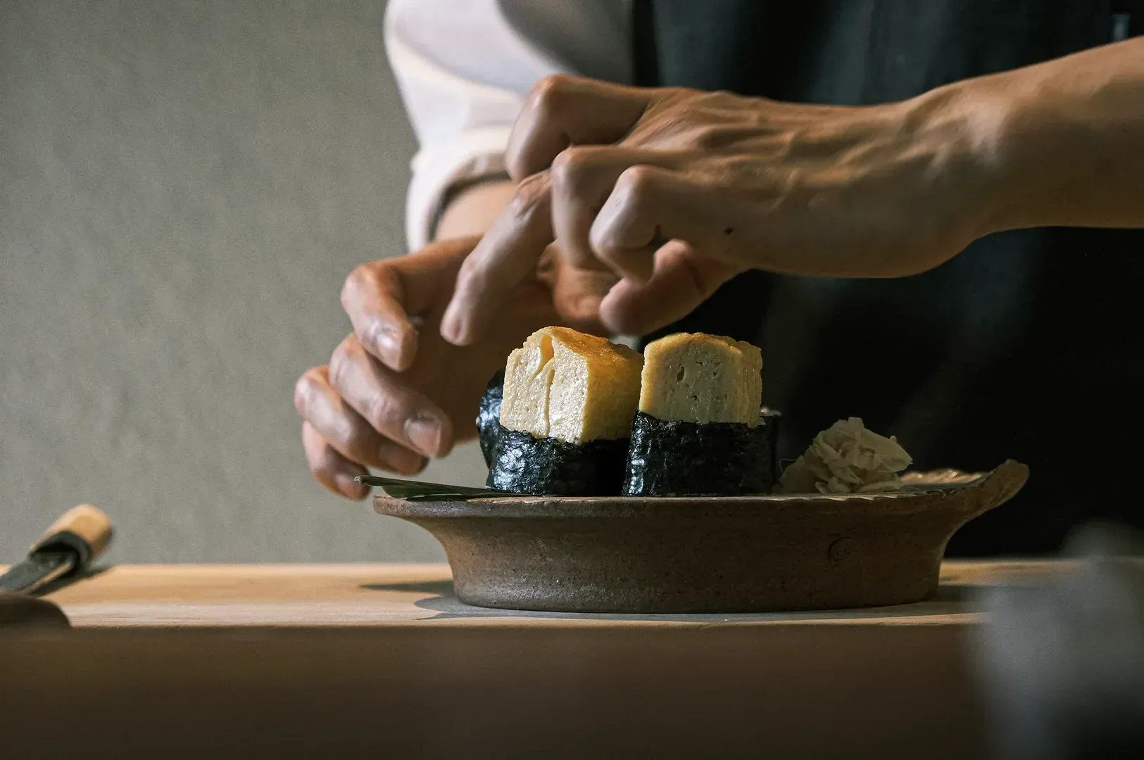 A chef's hands carefully plating tamago sushi, highlighting the intimate, unexpected kindness and dedication found in food service.