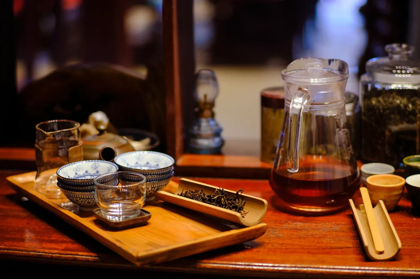 A close-up of a traditional tea ceremony setup featuring loose leaf tea, small ceramic bowls, and a glass pitcher on a wooden tray, creating an atmosphere of mindful presence and the practice of listening.