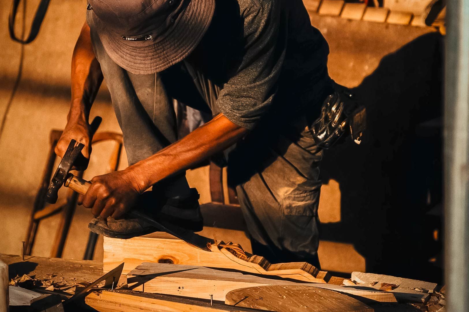 Woodworker carving a wooden piece by hand in a warm, sunlit workshop.