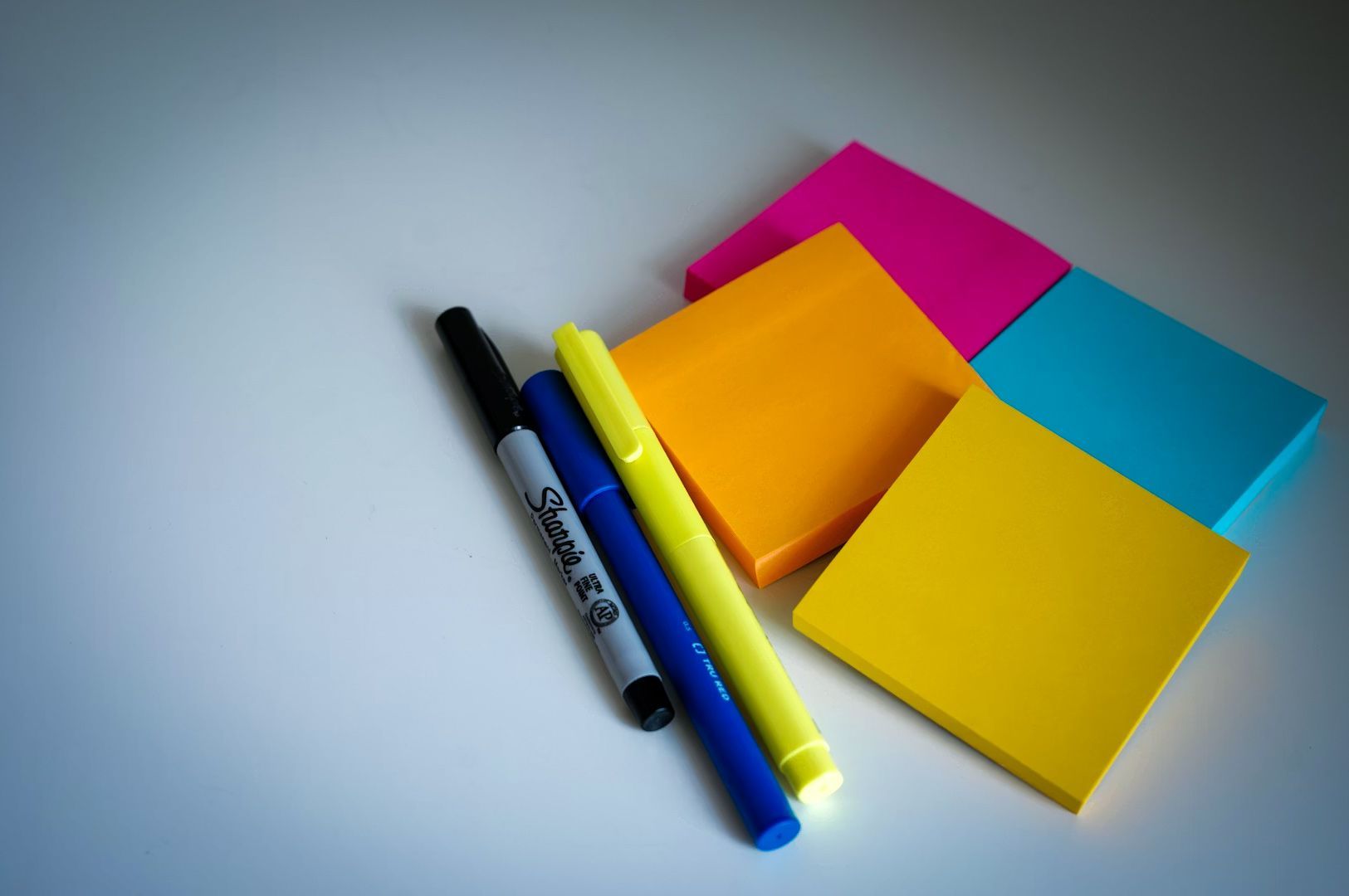 Colorful sticky notes arranged on a white desk alongside a black marker, blue pen, and yellow highlighter.