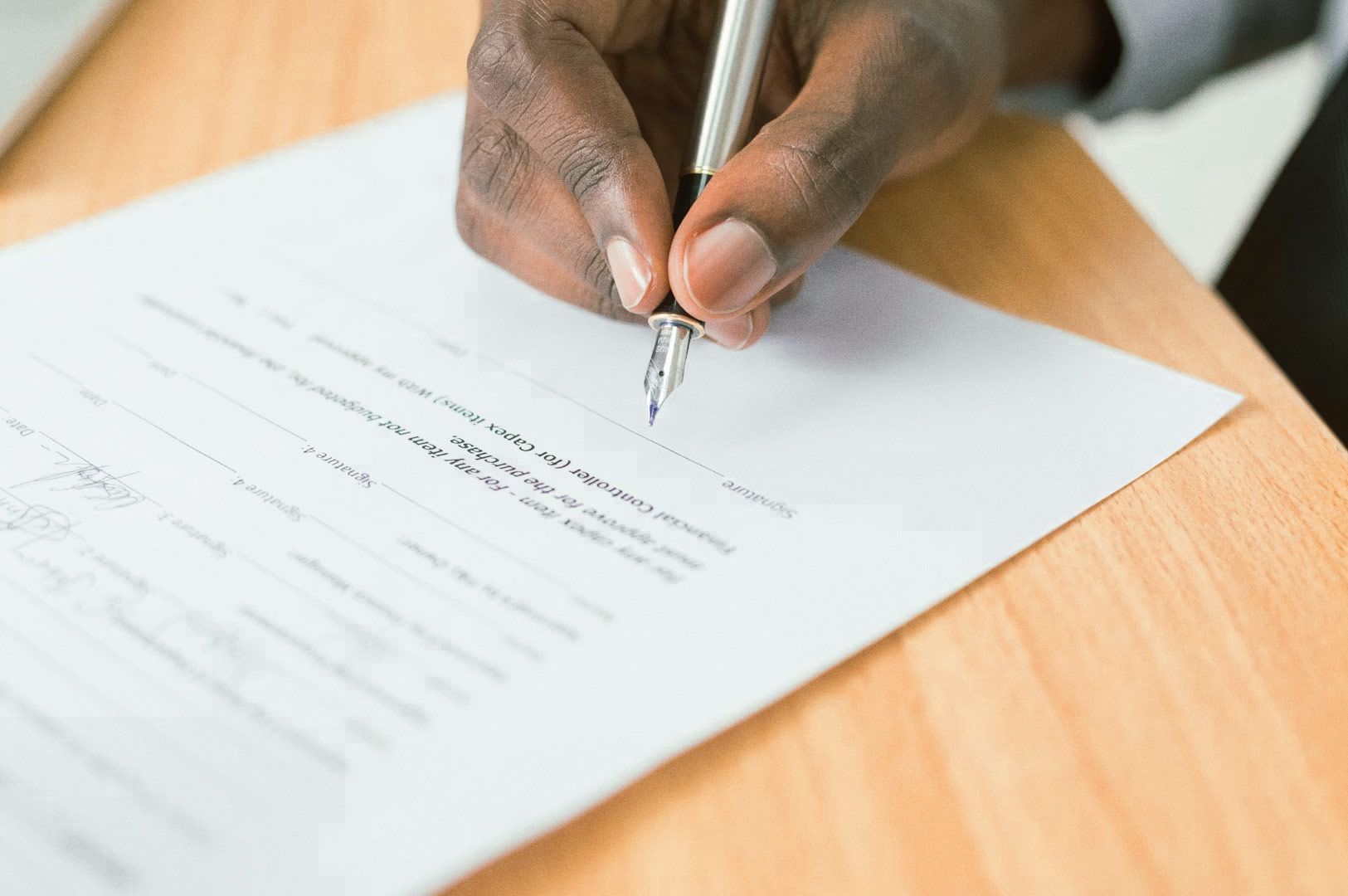 Hand signing a formal document with a pen on a wooden desk, representing contract approval, legal paperwork, or business documentation.