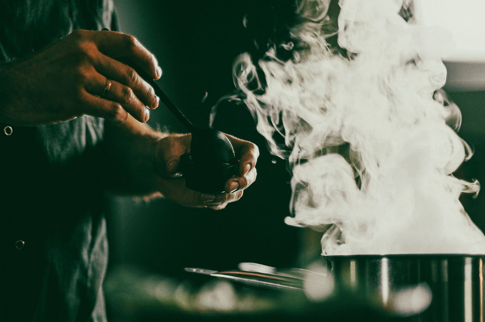 Hands holding a ladle near a steaming pot in a kitchen, with thick steam rising into the air.
