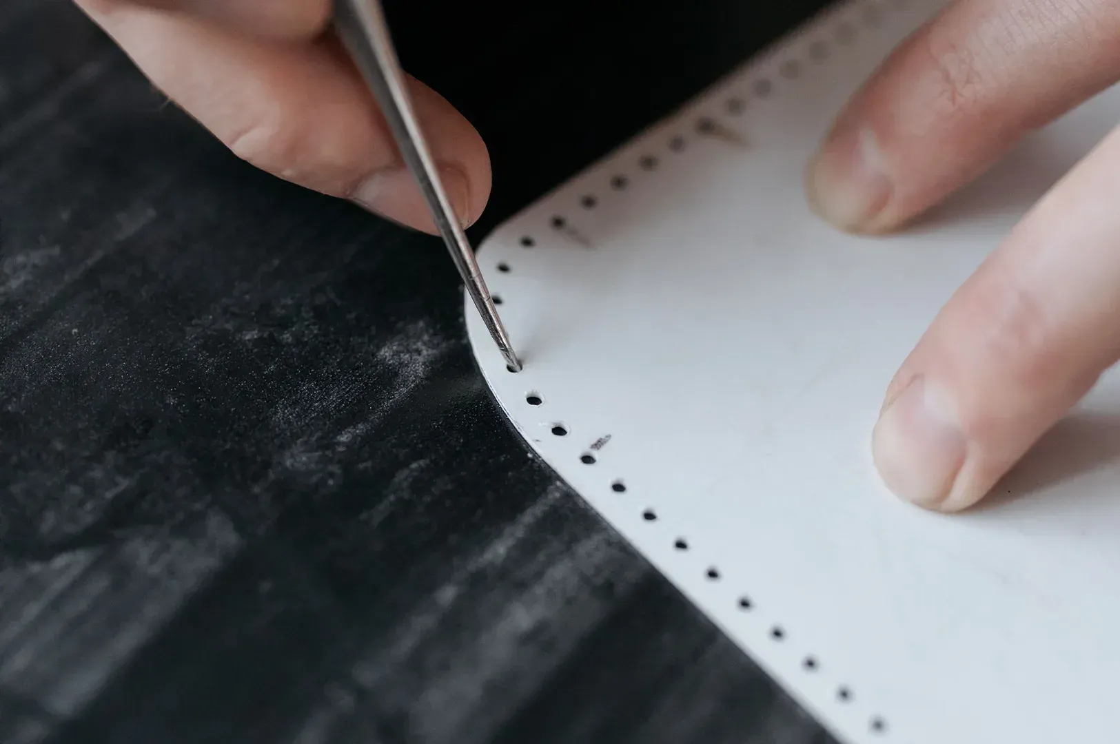 A focused, steady hand using a precision tool to mark consistent holes on a piece of material, illustrating how boundaries are practiced through small, deliberate, and rhythmic actions rather than conflict.