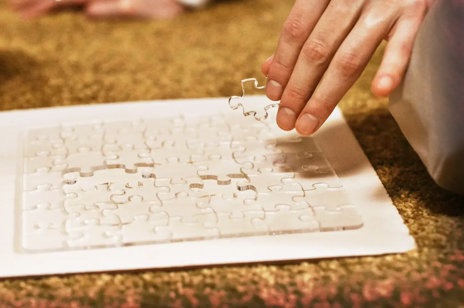 A close-up of a hand carefully placing a clear puzzle piece, symbolizing the patient act of doing and learning through the repetition required to master a complex apprenticeship.