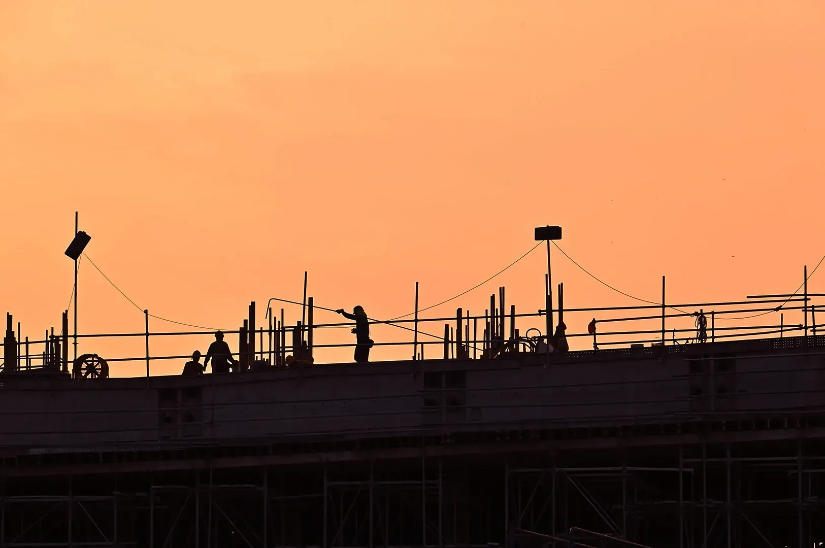 A silhouette of a team of construction workers on a scaffold against a vibrant sunset, illustrating the themes of collaborative effort, the discipline of maintenance, and the construction of long-lasting values.
