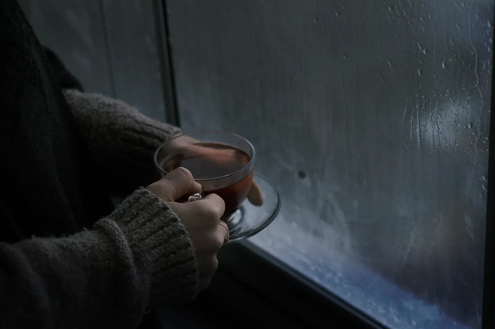 A person holding a warm cup of tea by a rainy window, embodying the quiet, reflective ritual of pausing to find clarity when everything feels important.