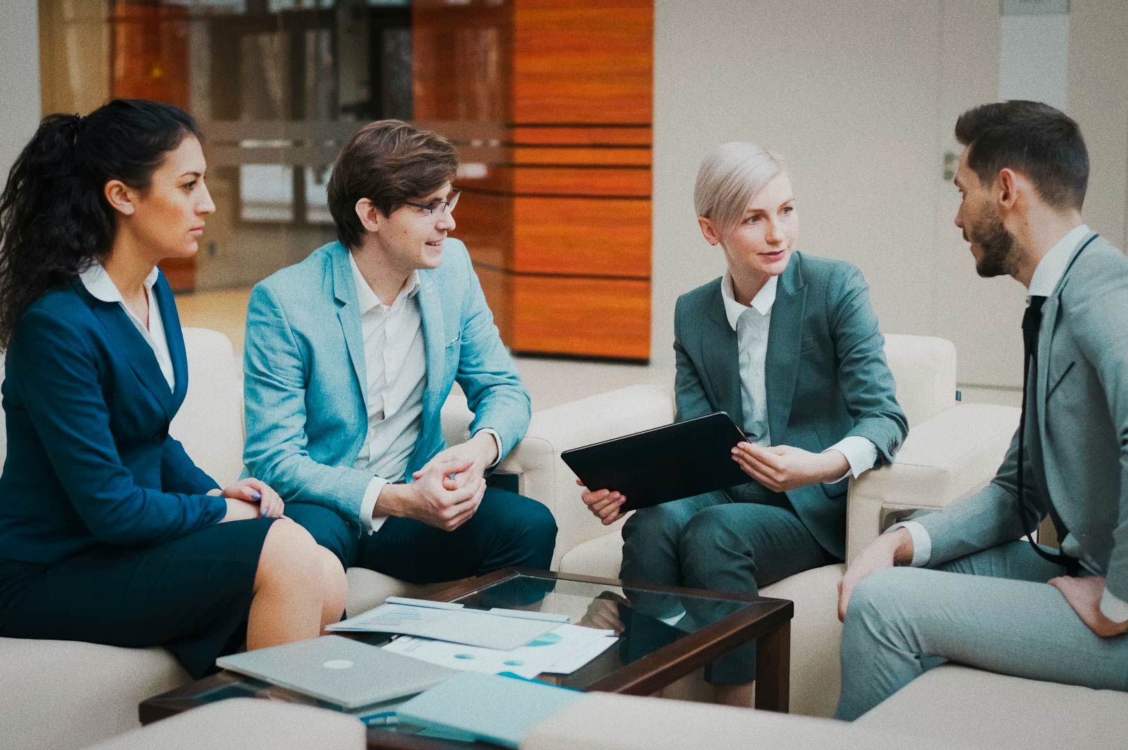 Business team engaged in collaborative discussion, tablet in hand, seated in contemporary office with wooden paneling.
