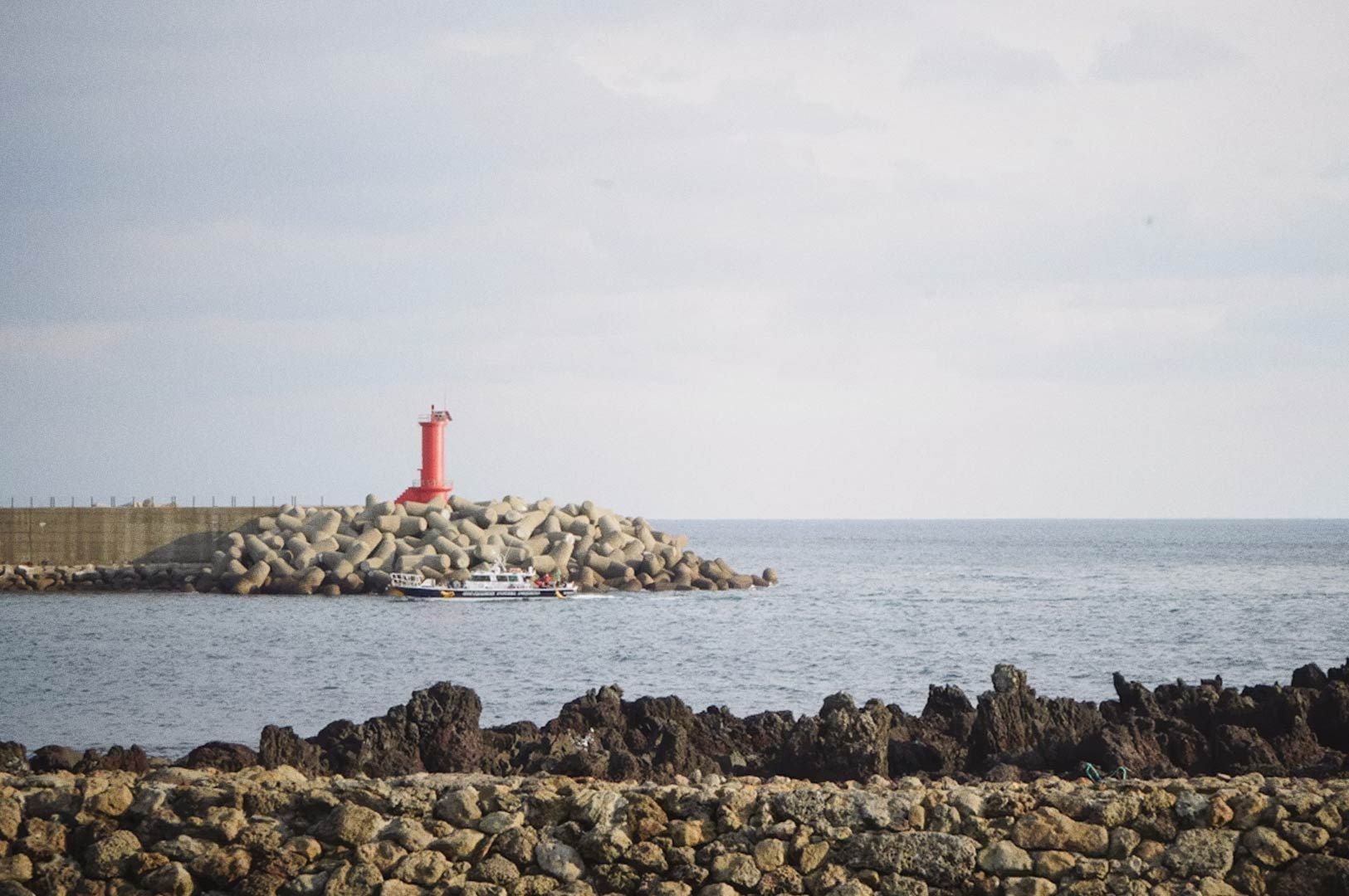 Red lighthouse on a rocky breakwater by the sea with a small boat nearby