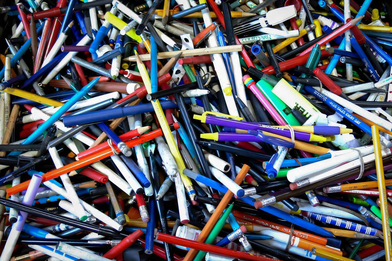 Colorful assortment of pens, pencils, and writing instruments scattered in a large pile.