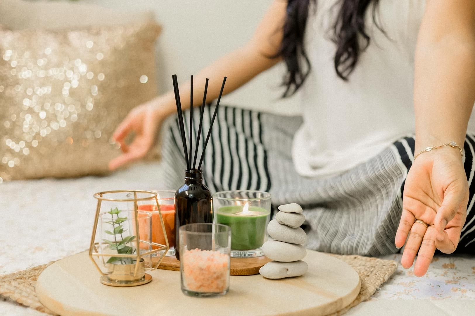 Person practicing meditation beside a tray of candles, aromatherapy oils, salt crystals, and stacked stones.